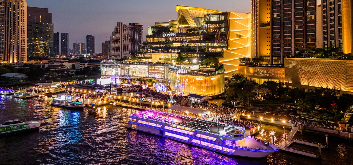 Современно освещенный фасад торгового комплекса ICONSIAM и пирс с причаливающими катерами. Самый популярный пункт отправления: футуристический комплекс ICONSIAM на западном берегу реки.